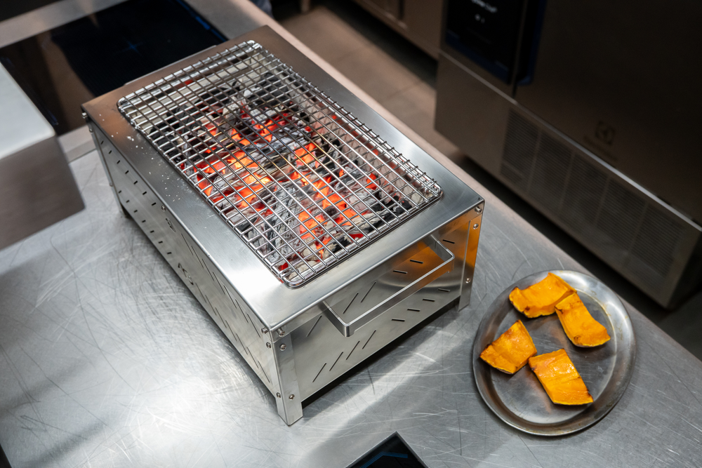 Nuova piastra filtracenere unica in acciaio refrattario

Un altro elemento apprezzato da Luca Marchini riguarda il fondo della camera di combustione.

Nella precedente versione della AG Grill XL era presente una griglia filtracenere rettangolare in ghisa, circondata da diversi elementi refrattari.

Nel nuovo modello 2027 questa configurazione è stata sostituita da un'unica piastra filtracenere in acciaio refrattario.

La soluzione elimina la precedente struttura composta da più elementi, semplificando le operazioni di rimozione e pulizia.

La maggiore semplicità costruttiva permette anche di accedere più facilmente al fondo della griglia quando è necessario effettuare la manutenzione.

È un aggiornamento che contribuisce a rendere l'attrezzatura più pratica e funzionale, soprattutto per un utilizzo frequente.

Sono state inoltre modificate le maniglie laterali, ora provviste di una curvatura che migliora la presa durante il sollevamento e la movimentazione della griglia a freddo.